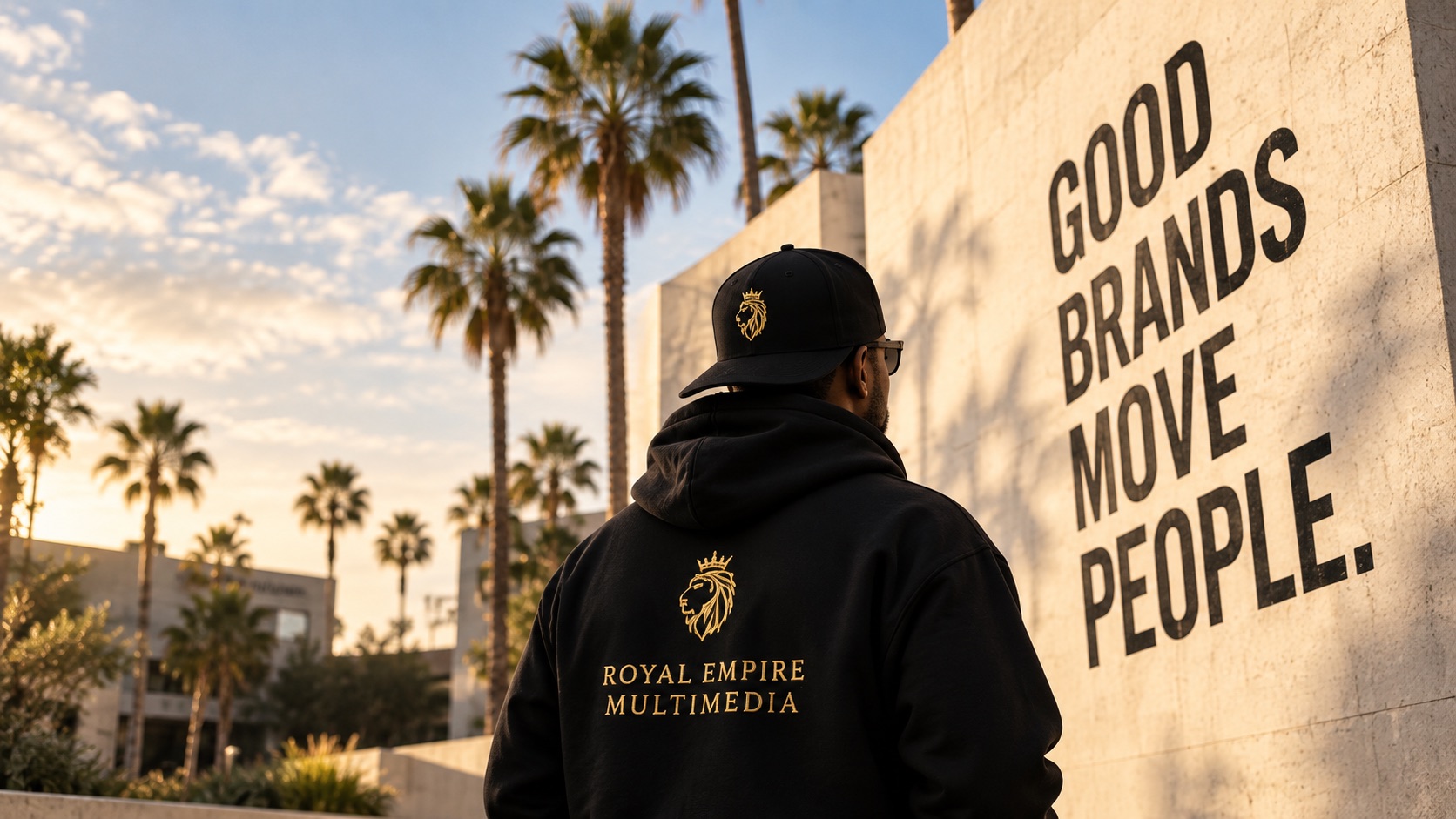 Royal Empire Multimedia hoodie beside a wall reading Good brands move people